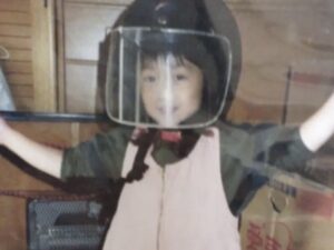 父のヘルメットを被って遊ぶ幼少の頃の久保まい